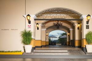 Die Vorderansicht des Occidental Papagayo Hotels mit einer gebogenen Eingangstür, einem Kronleuchter, zwei großen Pflanzen in weißen Töpfen und einem gepflasterten Eingang.