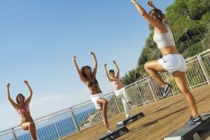 Vier Frauen machen Workout auf einer Terrasse mit Blick auf das Meer.