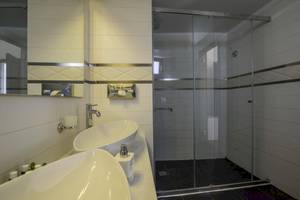 Badezimmer des La Mer Deluxe Hotel & Spa mit zwei Waschbecken, Glasdusche und Spiegel.