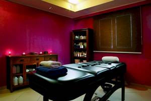 Massageraum im Olympia Golden Beach Resort mit roten Wänden, zwei Massagetischen, Kissen, Kerzen und einem Regal.
