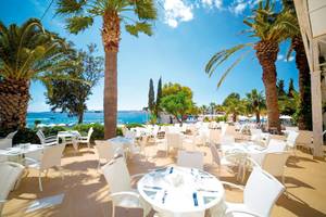 Außenbereich des LABRANDA TMT Bodrum Hotels mit vielen weißen Tischen und Stühlen, umgeben von Palmen und Blick auf das Meer.