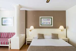 Ein schlichtes Hotelzimmer mit einem Bett, einem Sofa, Lampen und zwei Bilderrahmen an der Wand.