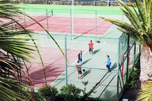 Tennisplatz im Hotel H10 Suites Lanzarote Gardens mit mehreren Spielern und Palmen im Hintergrund.