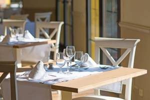 Ein gedeckter Tisch in einem hellen Restaurant mit Wein- und Wassergläsern, Besteck und Servietten.