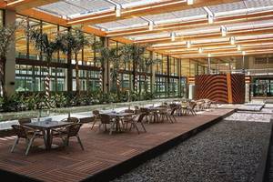 Innenhof des Nirvana Cosmopolitan Hotels mit Tischen und Stühlen, umgeben von Pflanzen und großen Fenstern.