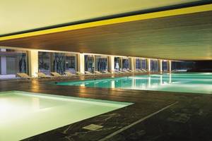 Innenpool des Nirvana Cosmopolitan Hotel mit Lounge-Sesseln und heller Beleuchtung.