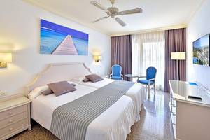 Hotelzimmer im MAC Puerto Marina mit zwei Betten, blauen Stühlen, Deckenventilator und Flachbildfernseher.