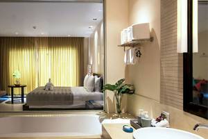 Badezimmer im Apsara Beachfront Resort und Villa mit Badewanne, Spiegel und Bett im Hintergrund.