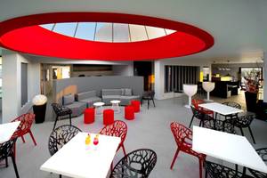 Innenbereich des Kipriotis Panorama Suites Hotels mit roten und schwarzen Stühlen, weißen Tischen und einer roten halbrunden Decke.