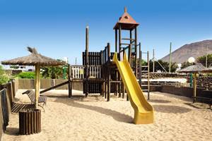 Spielplatz im Freien im Hotel SBH Royal Monica mit gelber Rutsche und Strohdach