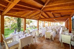 Innenbereich des Restaurants im Hipotels Natura Palace mit Holzbalken und grüner Rasenlandschaft im Hintergrund.