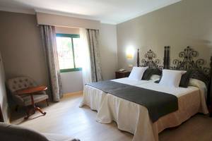 Doppelbettzimmer im Hipotels Natura Palace mit eleganter Einrichtung, zwei Betten, Nachttischen und einem Fenster mit Vorhängen.