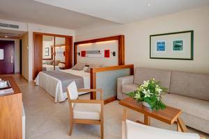 Innenansicht eines Hotelzimmers im Hipotels Natura Palace mit Bett, Sofa, Tisch und Fernseher.