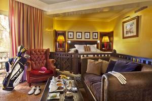 Zimmer im Palmeraie Palace Hotel mit Bett, Sofa, Tisch mit Essen und Golftasche.