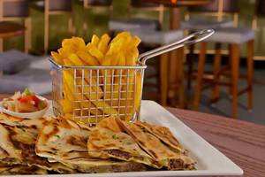 Ein Teller mit gegrillten Quesadillas, Beilagen und Pommes frites in einem Restaurant.