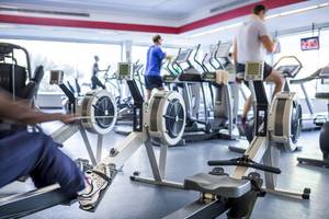 Fitnessstudio mit Rudergeräten und Laufbändern, mehrere Personen trainieren