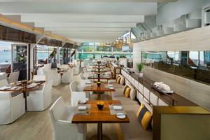 Innenansicht des Restaurants im Beach Rotana mit weißen Tischen und Stühlen und Blick auf das Meer.