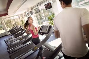 Frau im Fitnessstudio auf dem Laufband läuf, während ein Mann ihr zuschaut