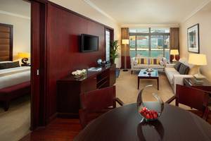 Innenansicht einer Suite im Beach Rotana Hotel mit Wohnzimmer, Schlafzimmer und Schreibtischbereich.