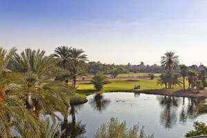 Aussicht auf den Golfplatz des Palmeraie Palace mit einem Golfwagen und einem See.
