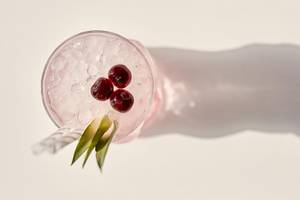 Cocktail mit Eis, roten Beeren und grünem Gras im Glas mit Schatten auf weißer Oberfläche
