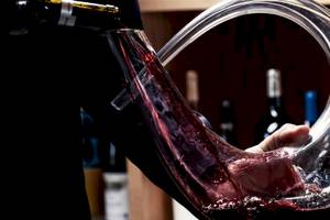 Person gießt Wein aus einer Flasche in ein geschwungenes Glas