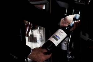 Ein Mann entkorkt eine Flasche Wein im Hotel Myconian Korali Relais & Chateaux.