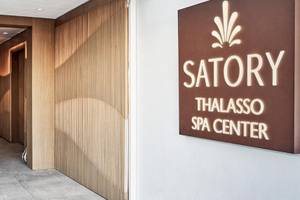 Eingang des Satory Thalasso Spa Center mit geometrischen Holzwänden und einem Schild, das den Namen des Spas anzeigt.