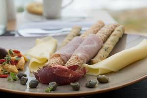 Ein Teller mit Käse, Aufschnitt, Oliven, Kapern und Gewürzen im Myconian Korali Hotel.