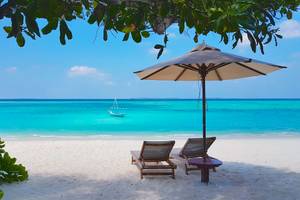 Strand mit Sonnenschirm, zwei Liegen und einem Boot im Wasser