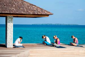 Fünf Personen, die Yoga auf der Terrasse des Barefoot Eco Hotels machen, mit Blick auf das Meer.