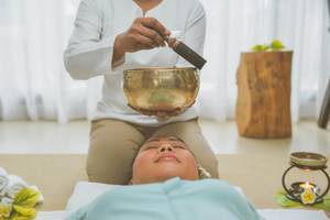 Massage im JW Marriott Mauritius Resort, eine Person wird massiert, während eine andere eine Glocke hält.