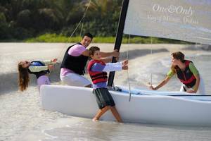 Eine Familie zieht ein Segelboot am Strand mit dem Hotelnamen The Palace At One & Only Royal Mirage, Dubai.