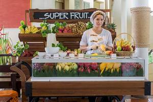 Frau am Cape Panwa Hotel, die eine Ananas schneidet, mit einem Obststand im Hintergrund.