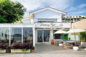 Außenansicht des The Trading Post Supermarkts mit Sitzplätzen und Sonnenschirmen.
