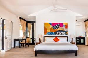 Schlafzimmer im Angsana Velavaru Hotel mit einem großen Bett, buntem Wandbild und weißen Wänden.