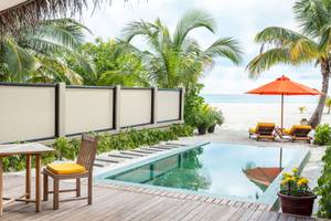 Außenbereich des Angsana Velavaru Hotels mit Pool, Tisch, Stühlen und Sonnenschirm am Strand