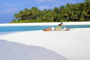Paar sitzt auf weißem Sandstrand und genießt ein Picknick im Freien.