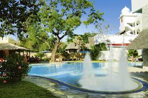 Der Swimmingpool-Bereich des Bamburi Beach Hotels mit zwei Wasserfontänen und umliegenden Gebäuden.