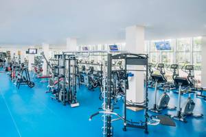 Fitnessstudio im Iberostar Paraiso del Mar Hotel mit vielen Geräten und blauen Böden.
