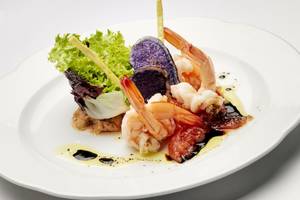 Elegantes Gericht mit Garnelen, Rotkohl und Beilagen auf einem weißen Teller.