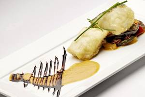 Gerecht auf weißem Teller mit Sauce und Gemüse, serviert mit Fisch.