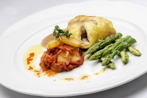 Ein Teller mit einem Gericht, bestehend aus einem gebackenen Teigtaschen, gebratenen Kartoffeln, Spargel und Sauce.