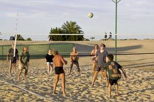 Gruppe von Spielern spielt Volleyball auf dem Sandstrand mit einem Netz.