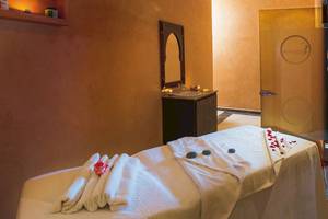 Massageraum im Hotel Pickalbatros Aqua Fun Club mit weißem Bett, Handtüchern, Rosenblättern und einem Spiegel.