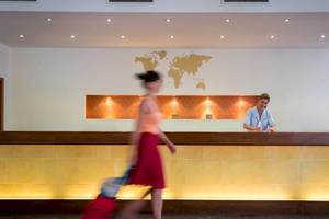 Eine Frau mit Koffern geht an der Rezeption des Bella Beach Hotels vorbei.