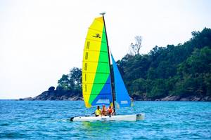 Drei Personen segeln auf einem bunten Segelboot auf dem Meer vor Kata Beach.