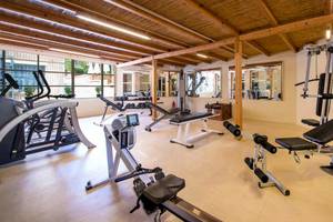 Fitnessraum im Bella Beach Hotel mit verschiedenen Trainingsgeräten und Holzbalkendecke.
