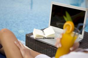 Frau am Pool mit Laptop und Buch