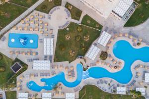 Luftaufnahme des Poolbereichs des Akti Imperial Deluxe Resorts mit zwei geschwungenen Pools, Sonnenliegen und Sonnenschirmen.